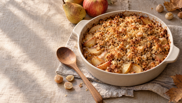 Golden apple and pear crumble with oats and chopped macadamias in a ceramic baking dish.