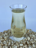 Clear glass vase filled with golden macadamia nut oil, surrounded by raw macadamia nuts on a light background.