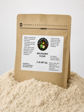 A 2 lb bag of Edgon Nuts Macadamia Flour standing upright in a mound of light beige flour against a clean white background.