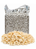 Raw macadamia nut pieces displayed in front of a large silver insulated bulk packaging bag on a white background.